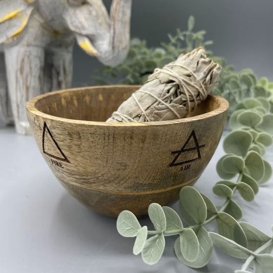 Wooden bowl with a smoldering sage bundle, surrounded by eucalyptus leaves on a neutral background.