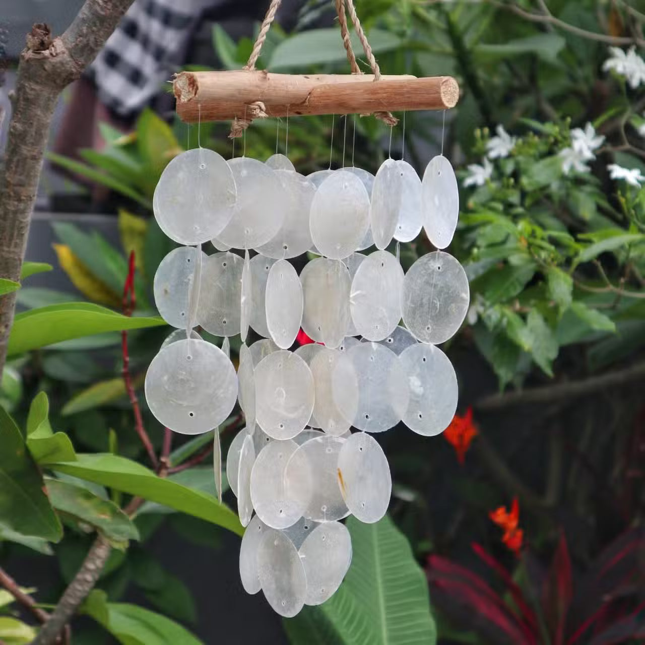 Decorative handmade wind chime with white glass discs hanging from a branch against a green foliage background
