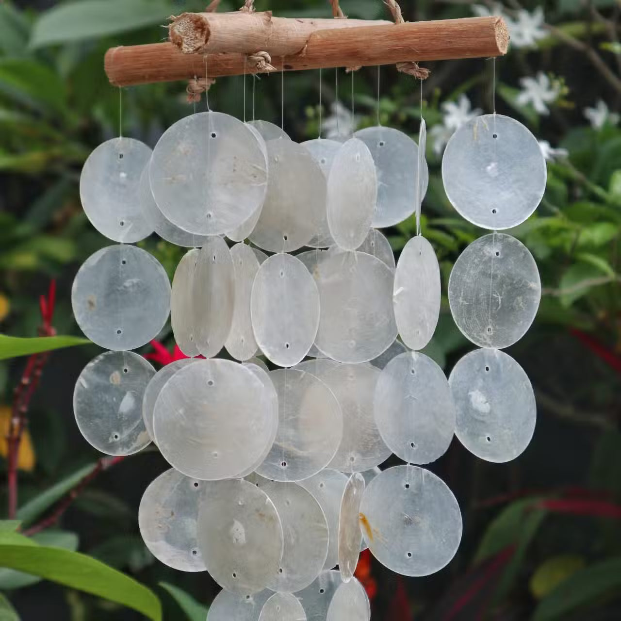 Decorative wind chime with clear circular recycled glass discs hanging from a branch against a natural background.